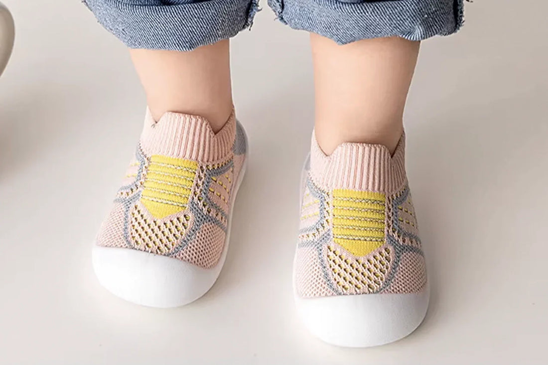 Pieds d’un bébé portant des chaussures tricotées roses et jaunes à semelles blanches.